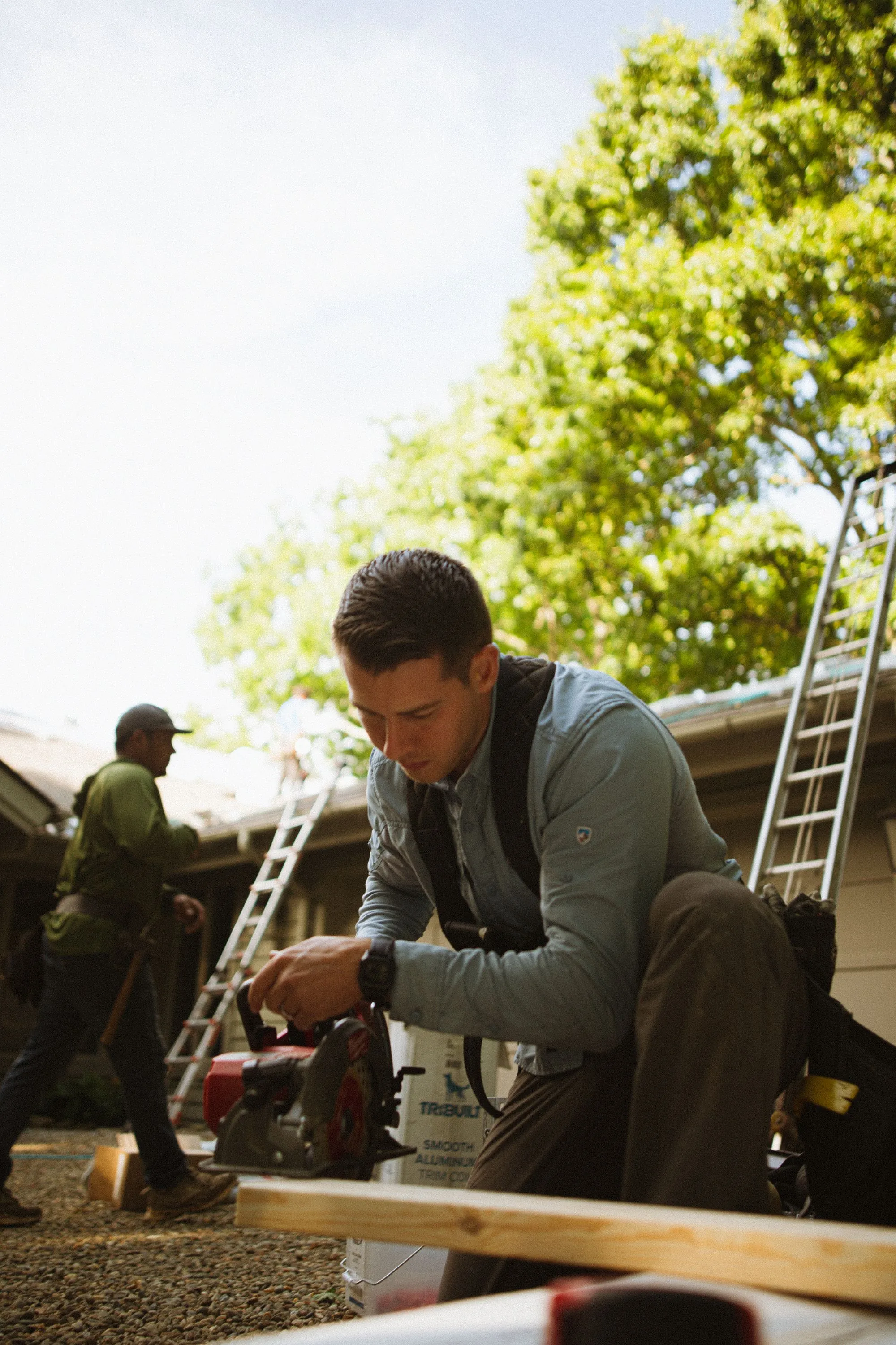 A worker outside a house with ladders set against the roof edge