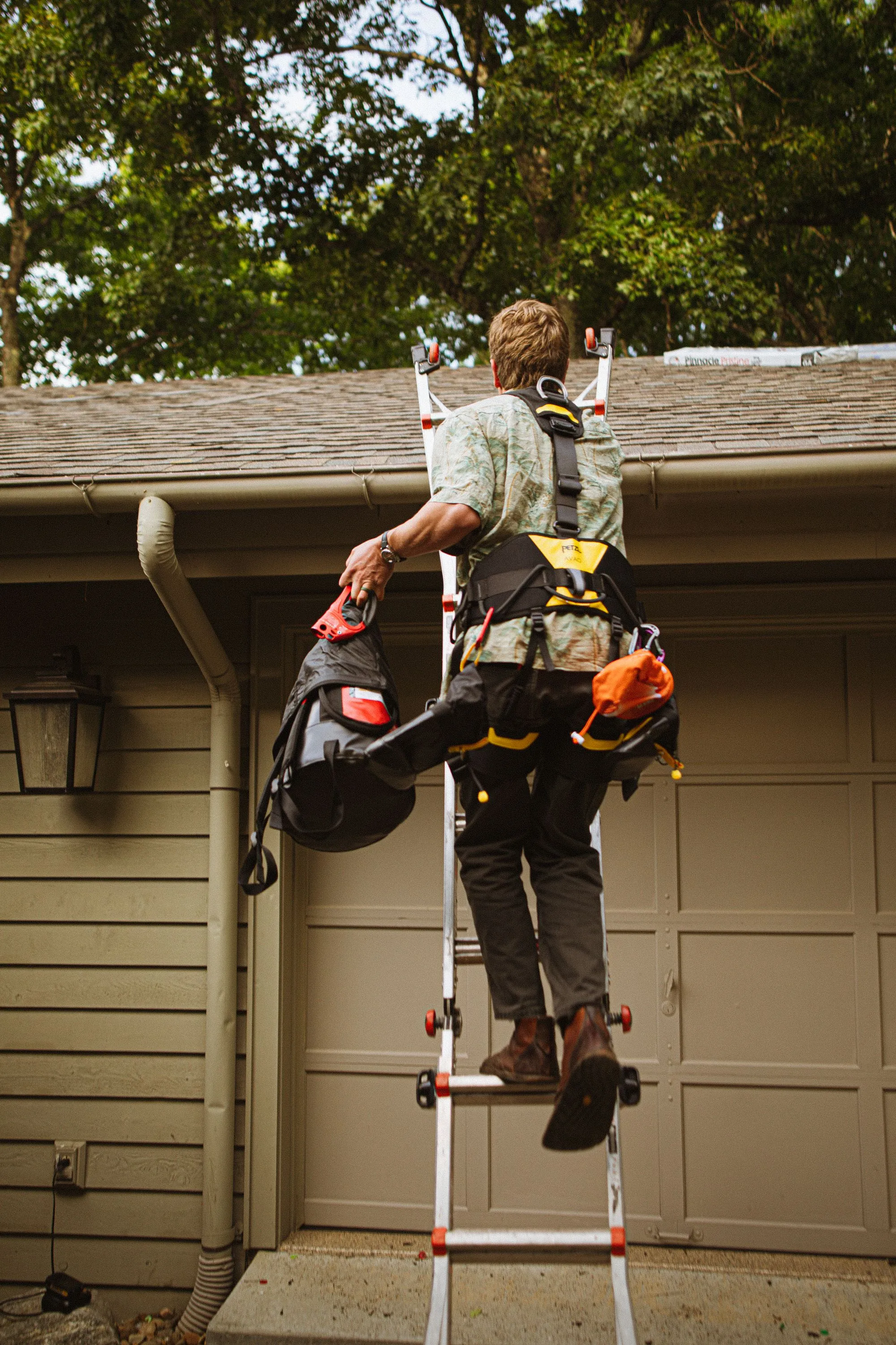A roofer putting on a safety harness beside a house