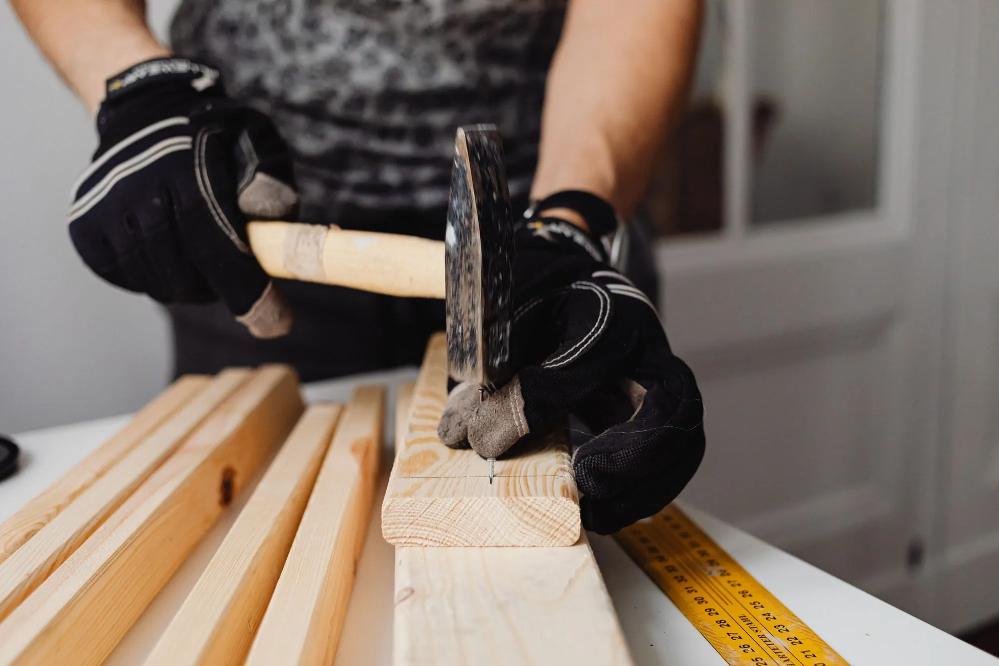 A hammer and nails in a worker's hands over fresh timber